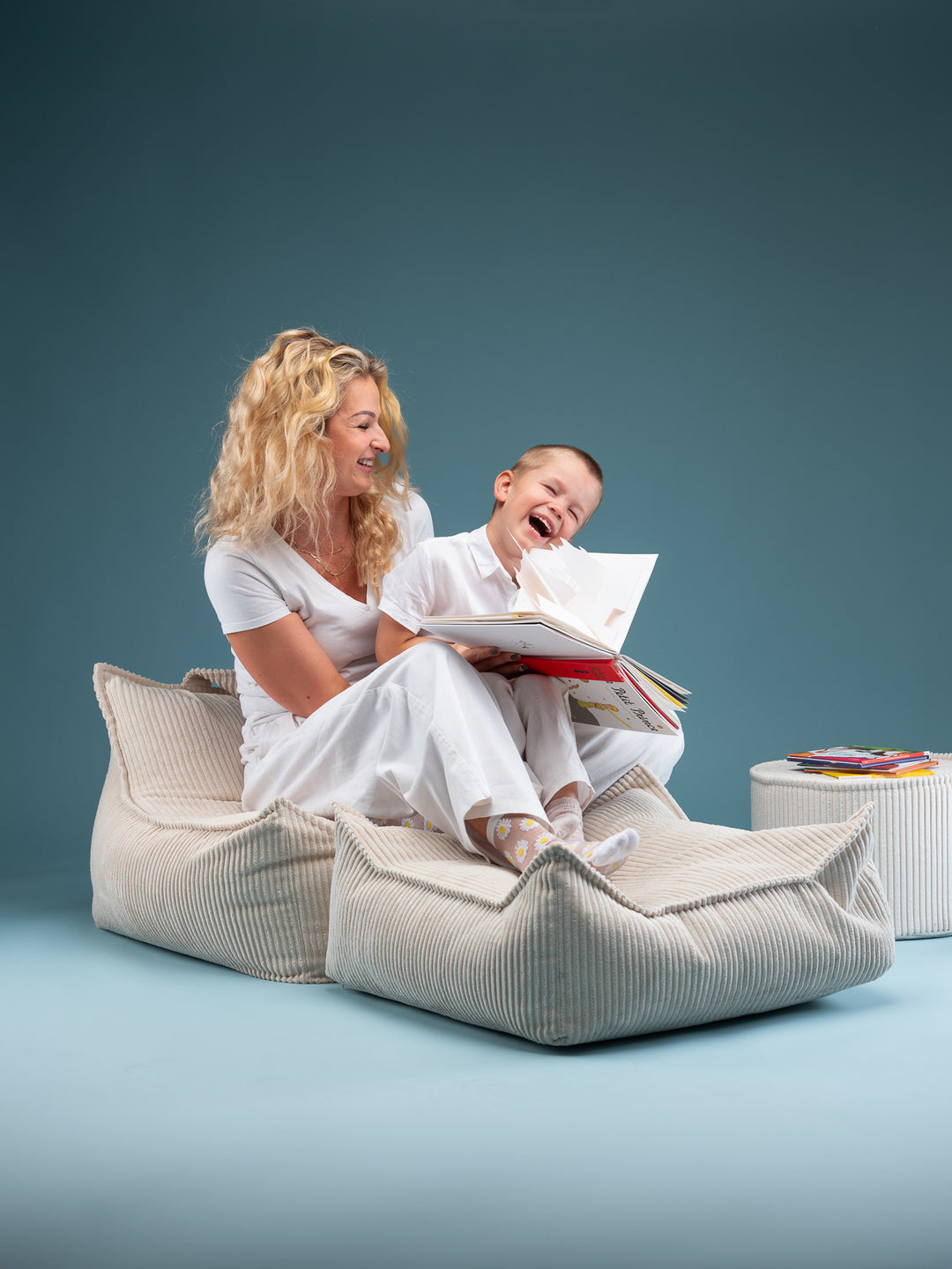 Adult and child reading together on cream Wigiwama beanbag with ottoman, teal backdrop