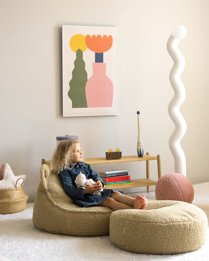 Child holding doll whilst sat in sage green Wigiwama bear chair, indoor lifestyle setting