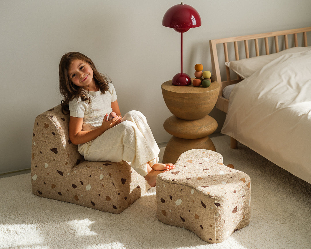 Girl on speckled chair beside bed, holding wooden bowl, bedroom portrait, Wigiwama