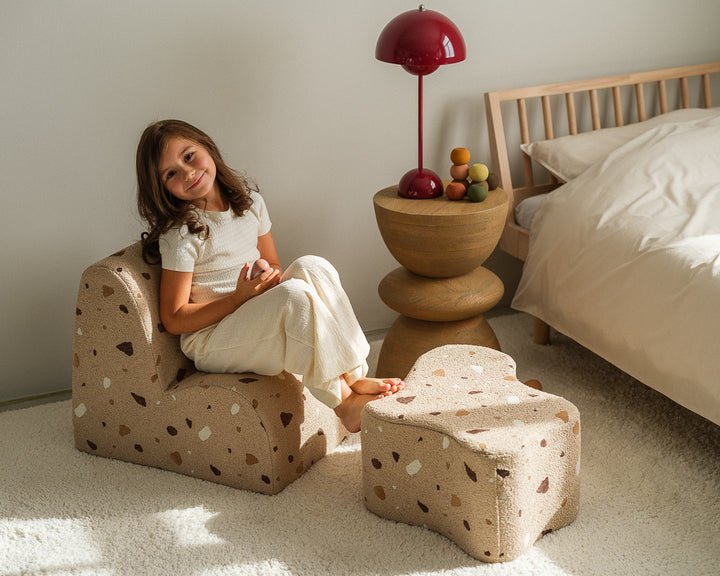 Girl on speckled chair beside bed, holding wooden bowl, bedroom portrait, Wigiwama