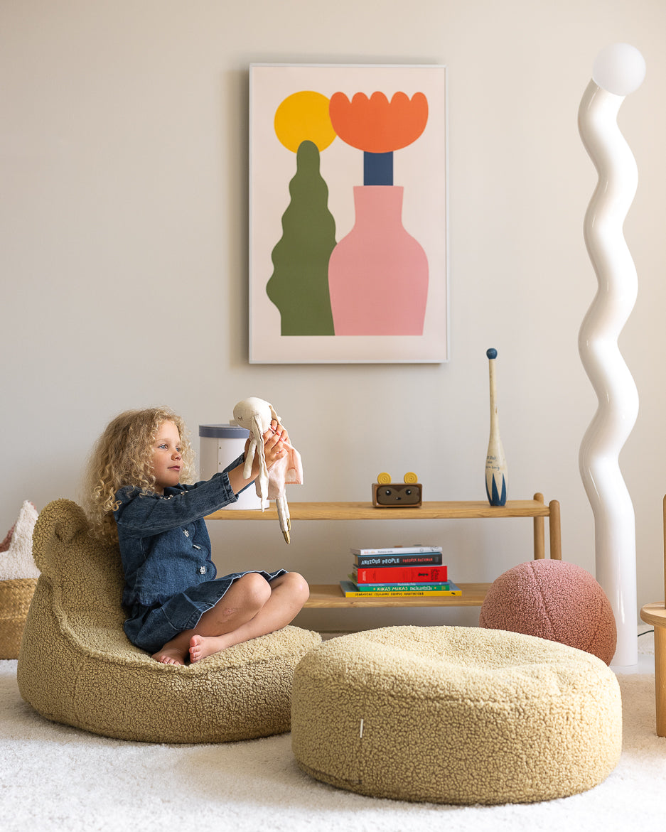 Child seated in sage green Wigiwama bear chair with feet on round ottoman in modern bedroom