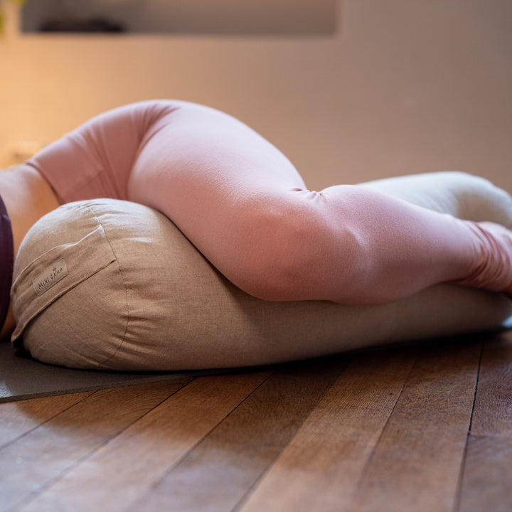 Close-up of legs resting against a MINICAMP Dusty Pink linen yoga bolster during a restorative stretch