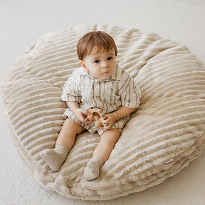Baby sitting on the MINICAMP ecru corduroy floor cushion holding a wooden toy