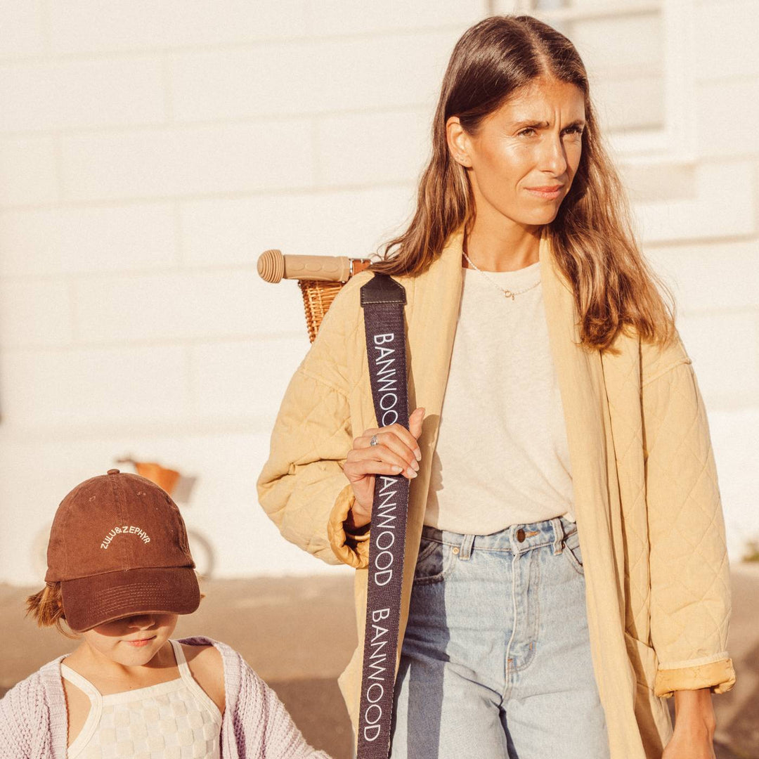 Woman using black carry strap to carry child on shoulders at beach location
