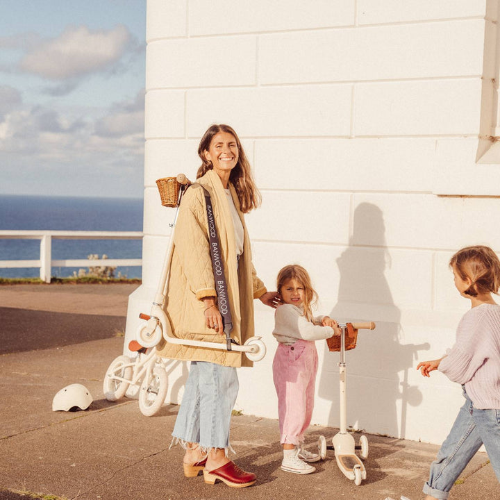 Woman wearing black carry strap with woven basket near seafront with children