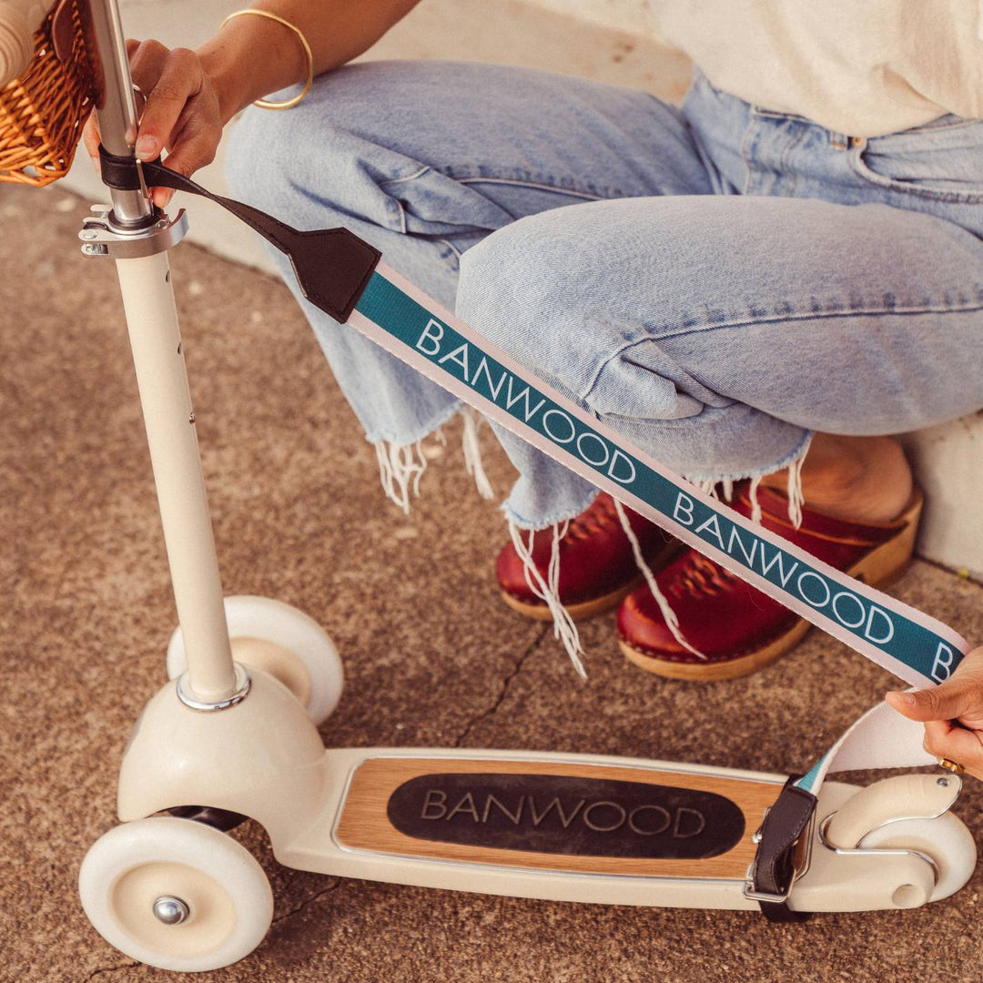 Person holding cream balance bike with attached teal carry strap, Banwood