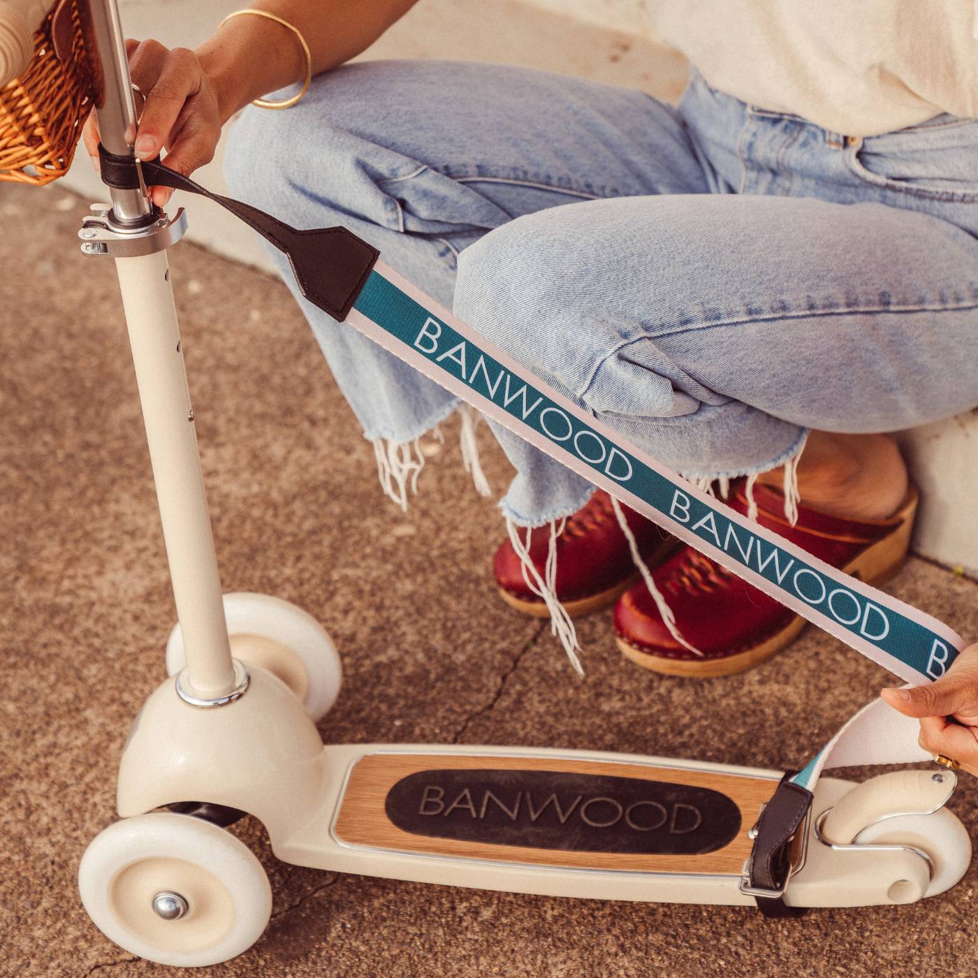 Person holding cream balance bike with attached teal carry strap, Banwood