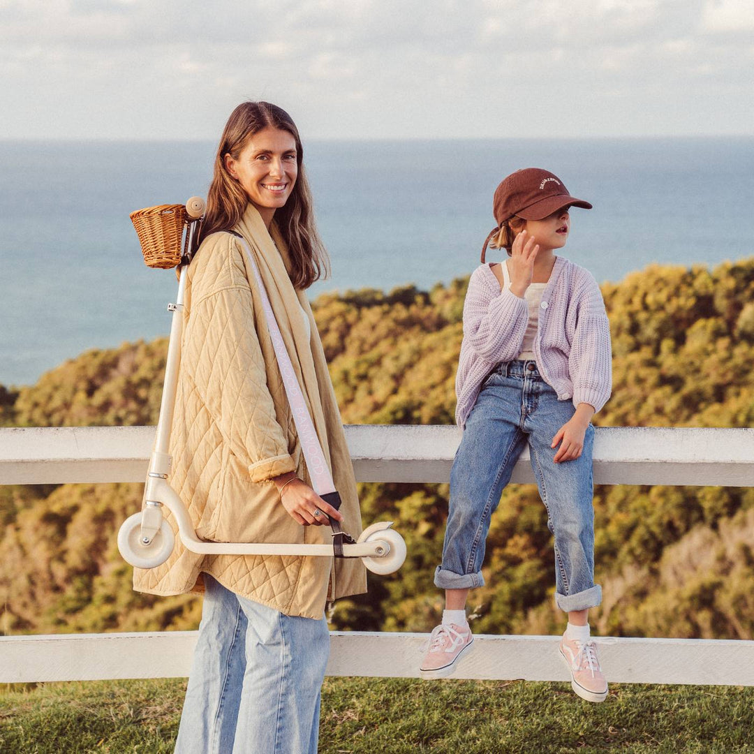Lifestyle photo: woman carrying cream scooter with pink strap by coastal cliff