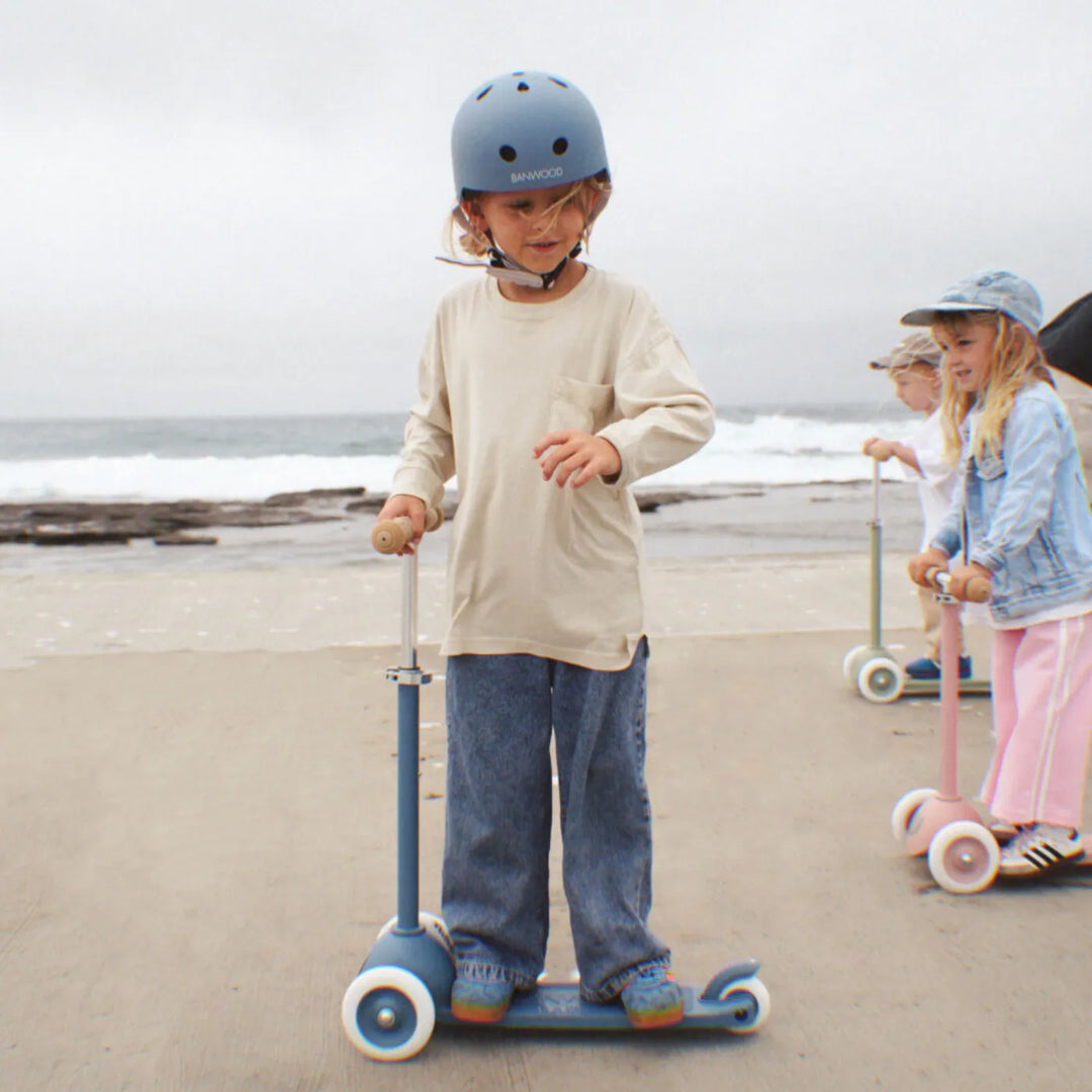 Child in helmet riding scooter on sandy beach with other children in background