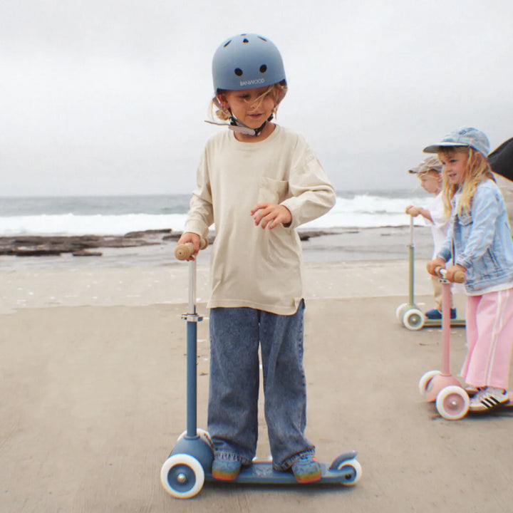 Child in helmet riding scooter on sandy beach with other children in background