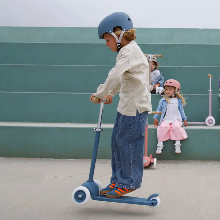 Adult in motion on scooter with helmet, riding past seated children in outdoor setting
