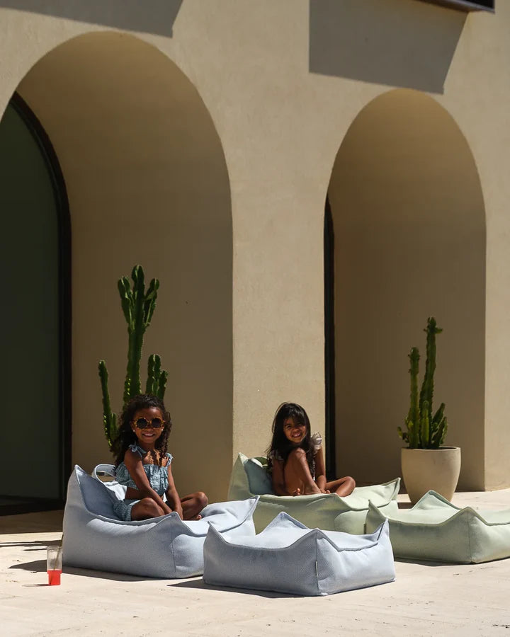 Children relaxing in beanbag chairs near arches with cacti in sunlit outdoor space