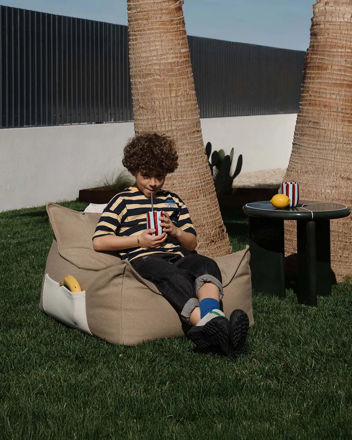 Child relaxing in beige bean bag chair with drink, garden setting