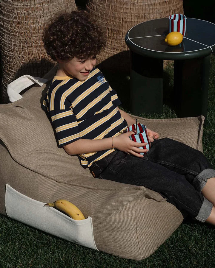 Child relaxing in beige bean bag chair in garden, lifestyle shot