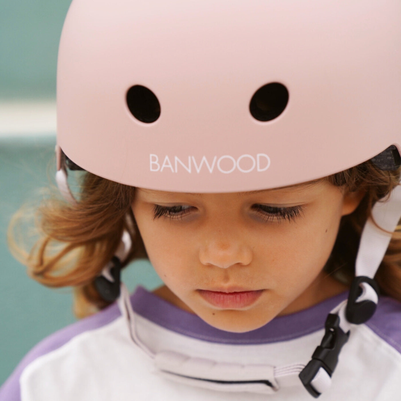 Child wearing pink safety helmet by water, showing proper fit and wear Banwood