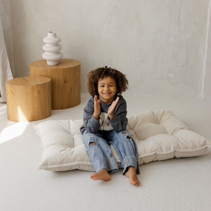 Child clapping while sitting on the MINICAMP ecru floor cushion folded upright as a backrest