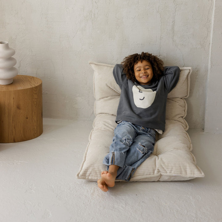 Child relaxing against the MINICAMP ecru floor cushion folded upright as a backrest