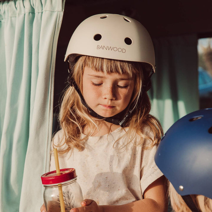 Child wearing cream Banwood helmet indoors by window, lifestyle setting
