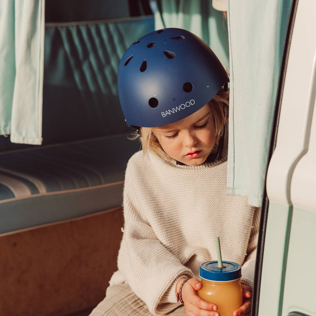 Child wearing navy safety helmet indoors with drink, lifestyle shot Banwood