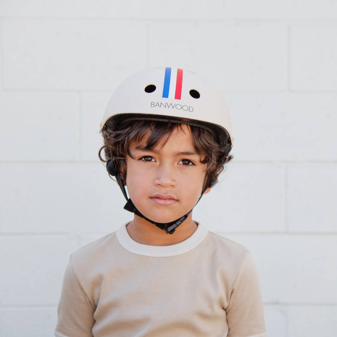 Child in cream Banwood striped helmet, front-facing pose against white wall