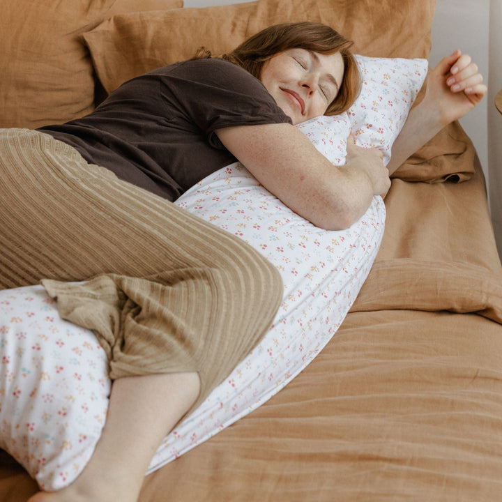 Woman hugging the MINICAMP Full Body Pillow with Milk White floral organic cotton cover on a sofa