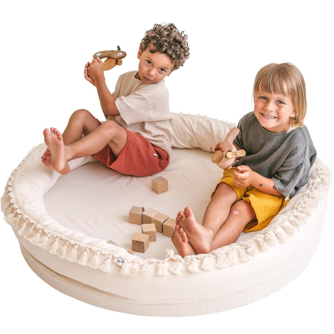 Two children playing with wooden toys inside the MINICAMP Large Round Nest Play Mat in Ecru