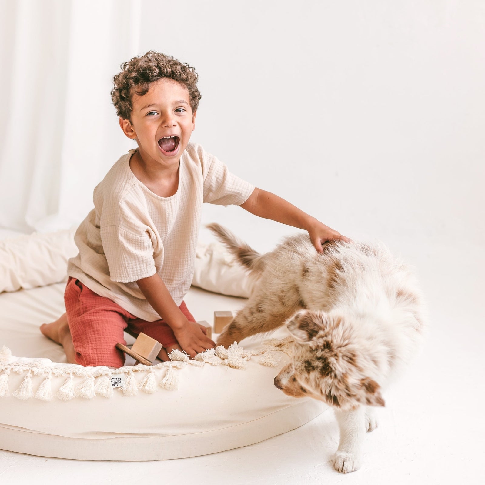 A child laughing while petting a dog on the MINICAMP Large Round Nest Play Mat in Ecru