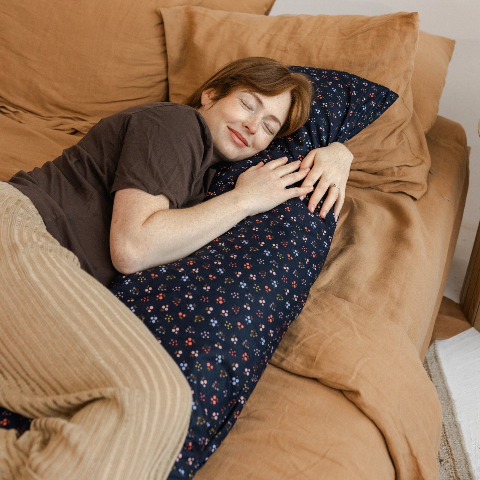 Woman hugging the MINICAMP Long Maternity and Lumbar Support Pillow, navy blue floral organic cotton cover, close up