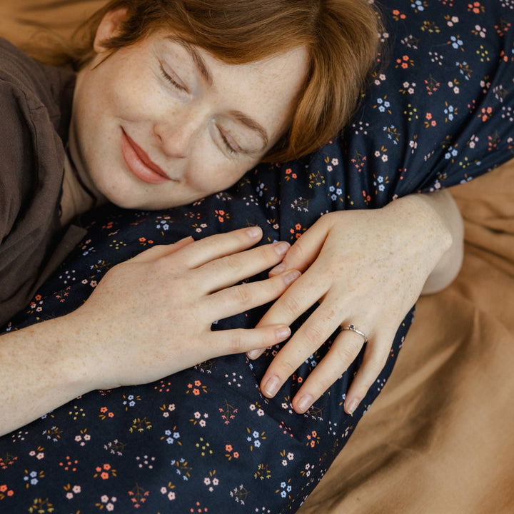 Close up of a woman resting against the MINICAMP Long Maternity and Lumbar Support Pillow, navy blue floral organic cotton cover