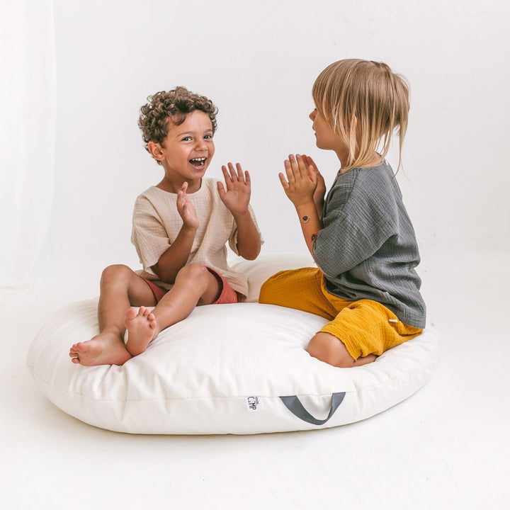 Two children sitting on the MINICAMP lounger floor pillow with carry handle