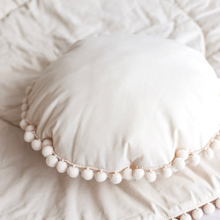 MINICAMP Throw Pillow in Ecru with Pompom Trim styled on a bed