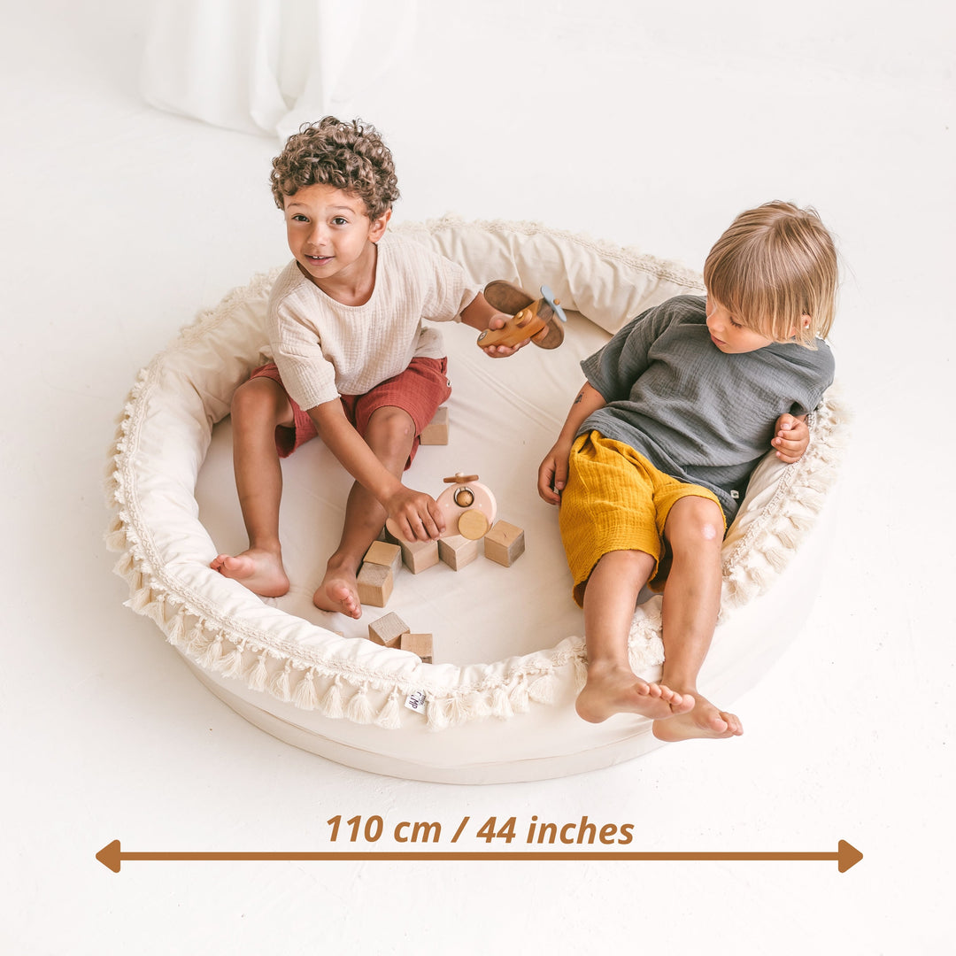 Two children playing inside the MINICAMP Large Round Nest Play Mat in Ecru, shown at approximately 105cm across