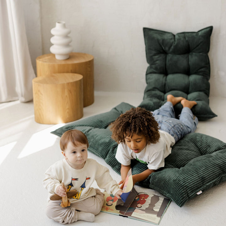 Two children playing beside the MINICAMP petrol green floor cushion folded upright as a backrest