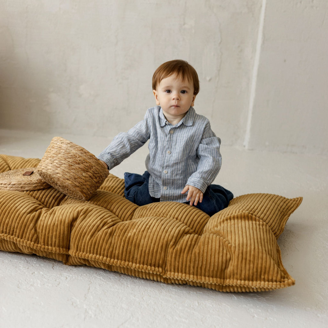 Child relaxing against the MINICAMP mustard floor cushion folded upright as a backrest