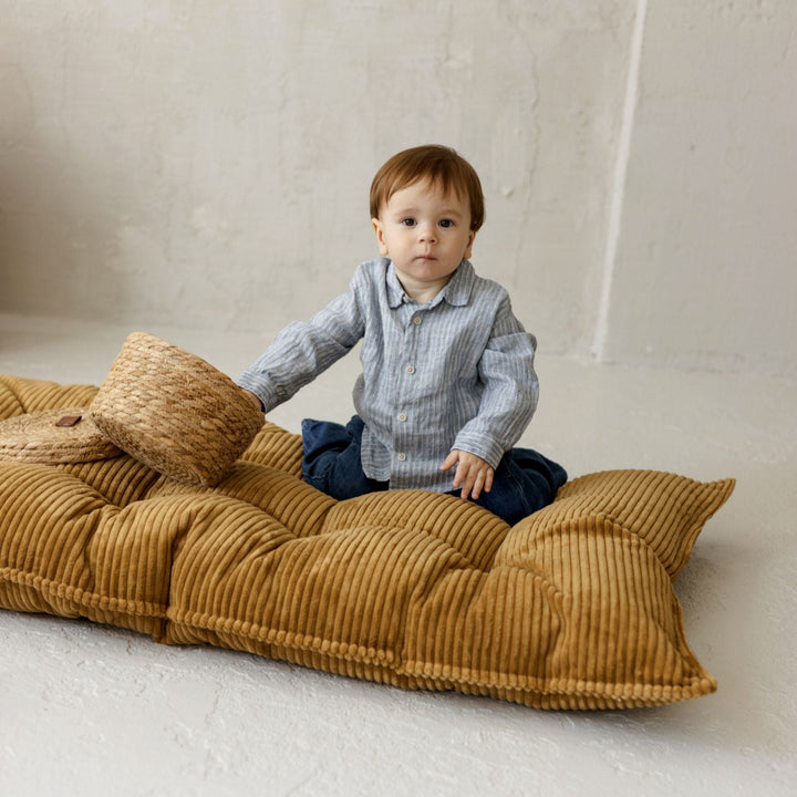 Child relaxing against the MINICAMP mustard floor cushion folded upright as a backrest