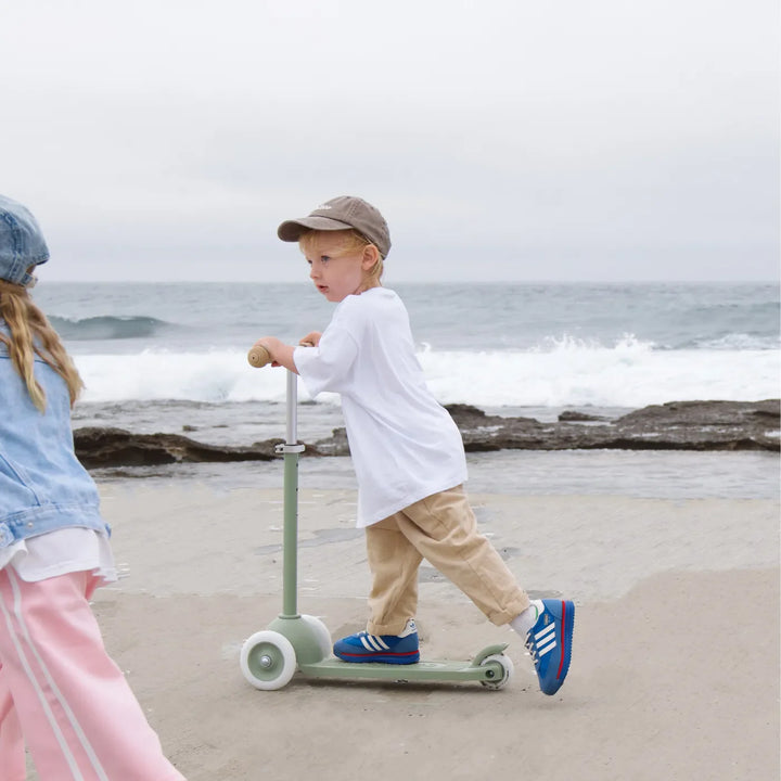 Child scooting on olive scooter at beach with ocean and waves in background