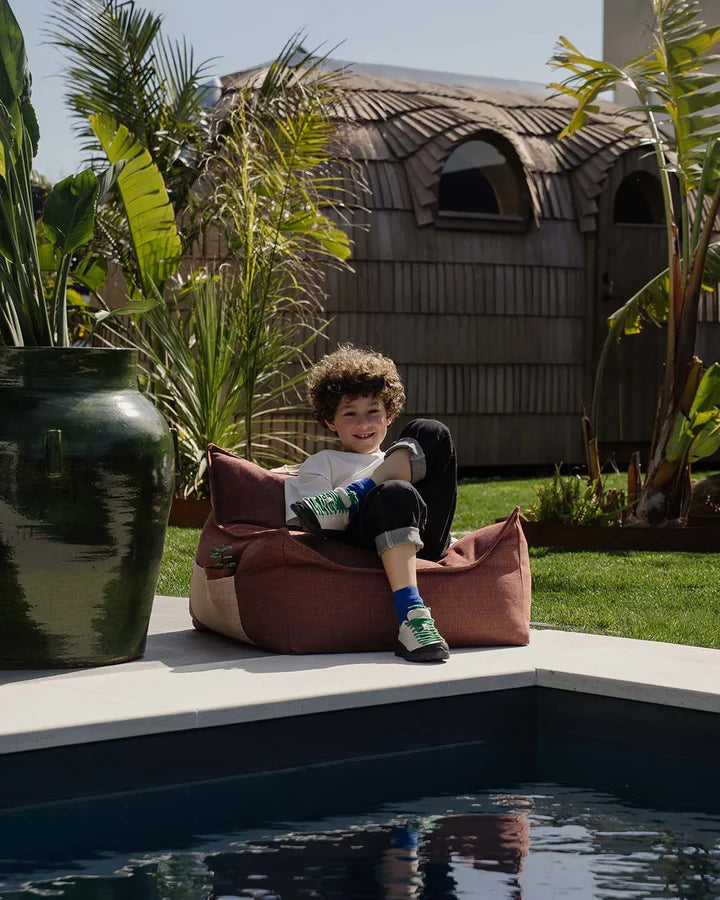 Child playing in burgundy bean bag chair by poolside