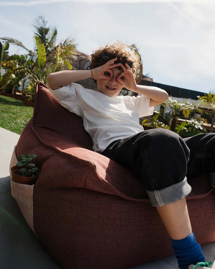 Child reading in pink bean bag chair in tropical garden setting