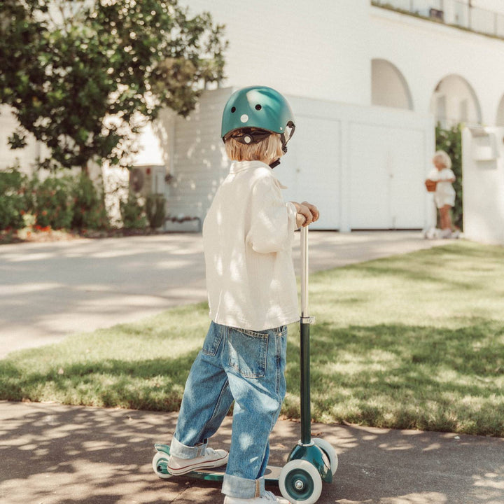 Child riding green Banwood scooter in helmet on driveway