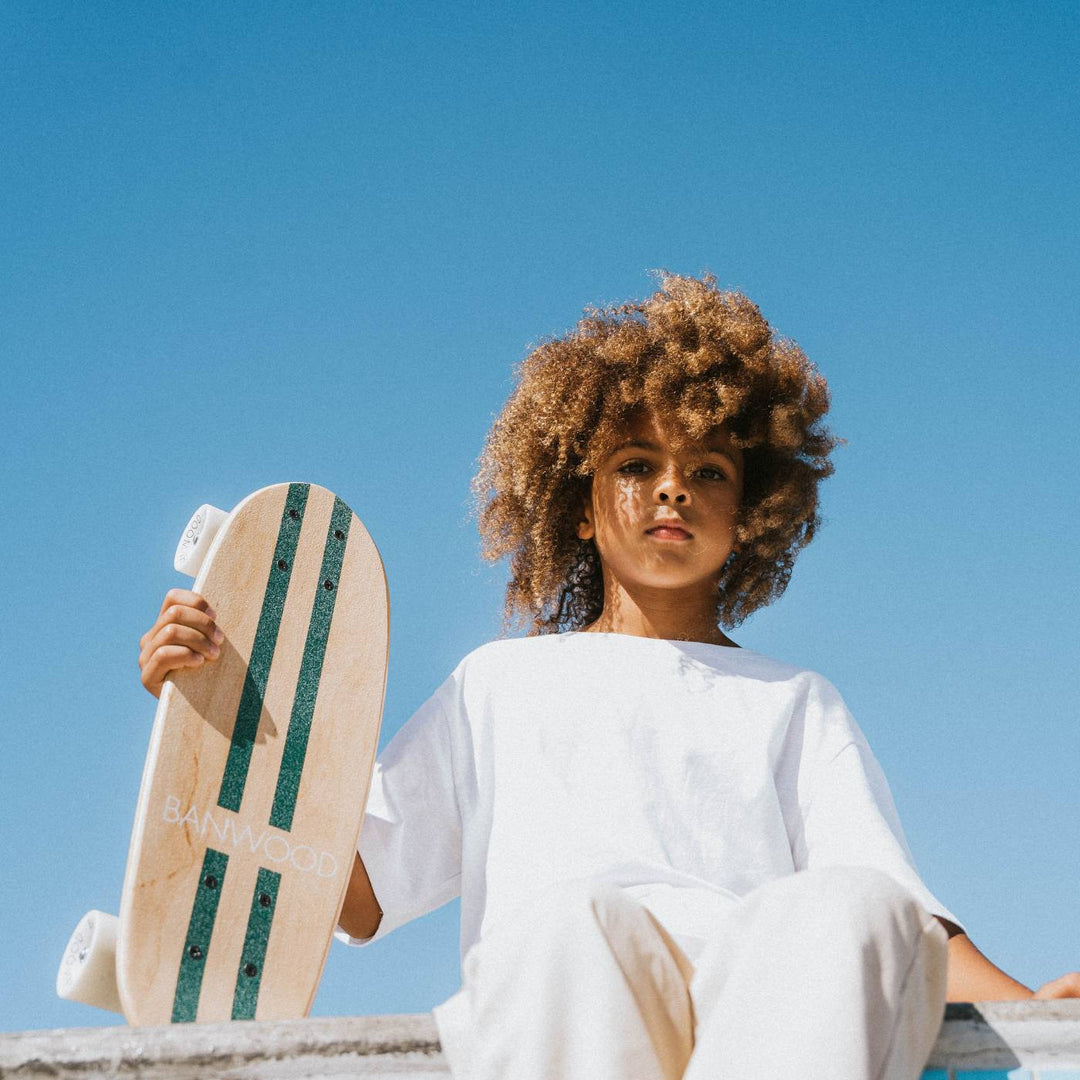 Child holding Banwood skateboard outdoors against clear blue sky