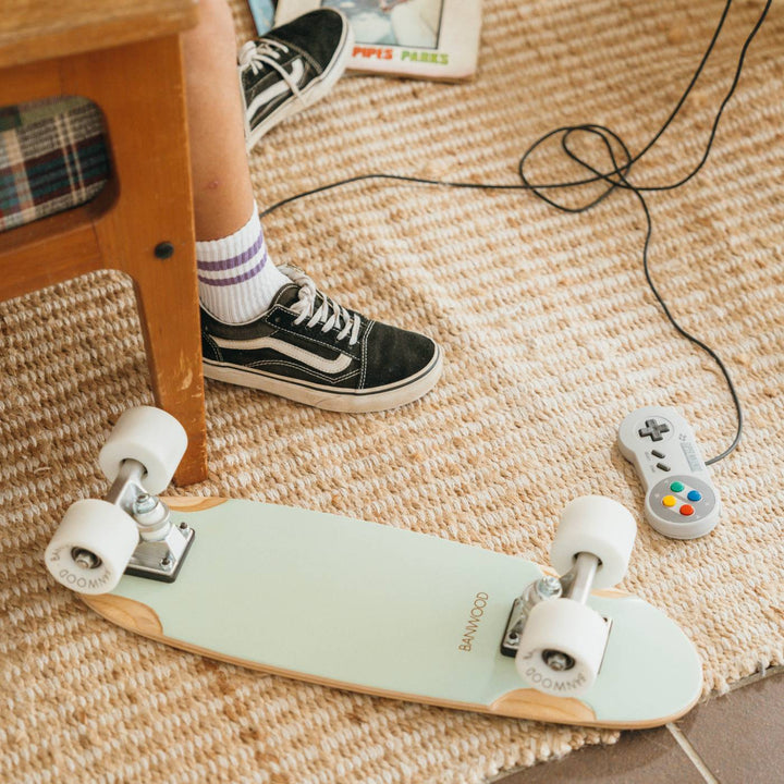 Mint skateboard on carpet during indoor play, child in black trainers nearby