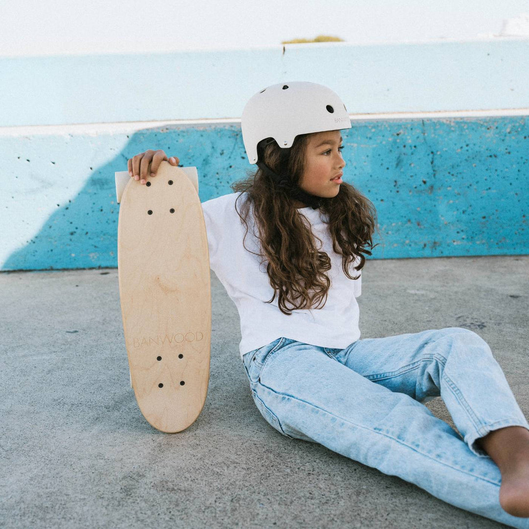 Child in white helmet holding Banwood skateboard at skate park