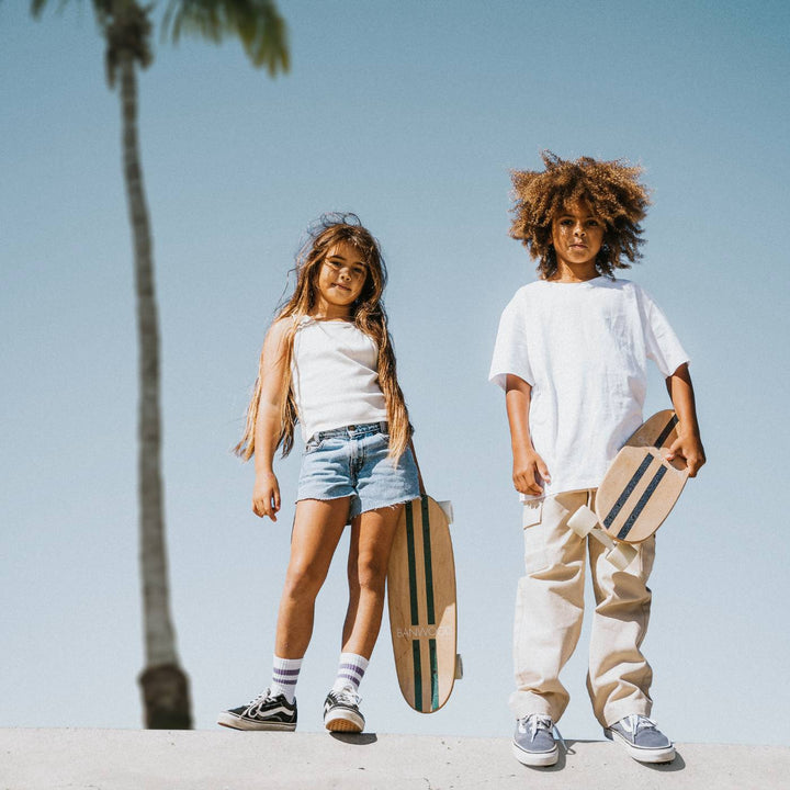 Two children posing outdoors with Banwood skateboards in sunny setting