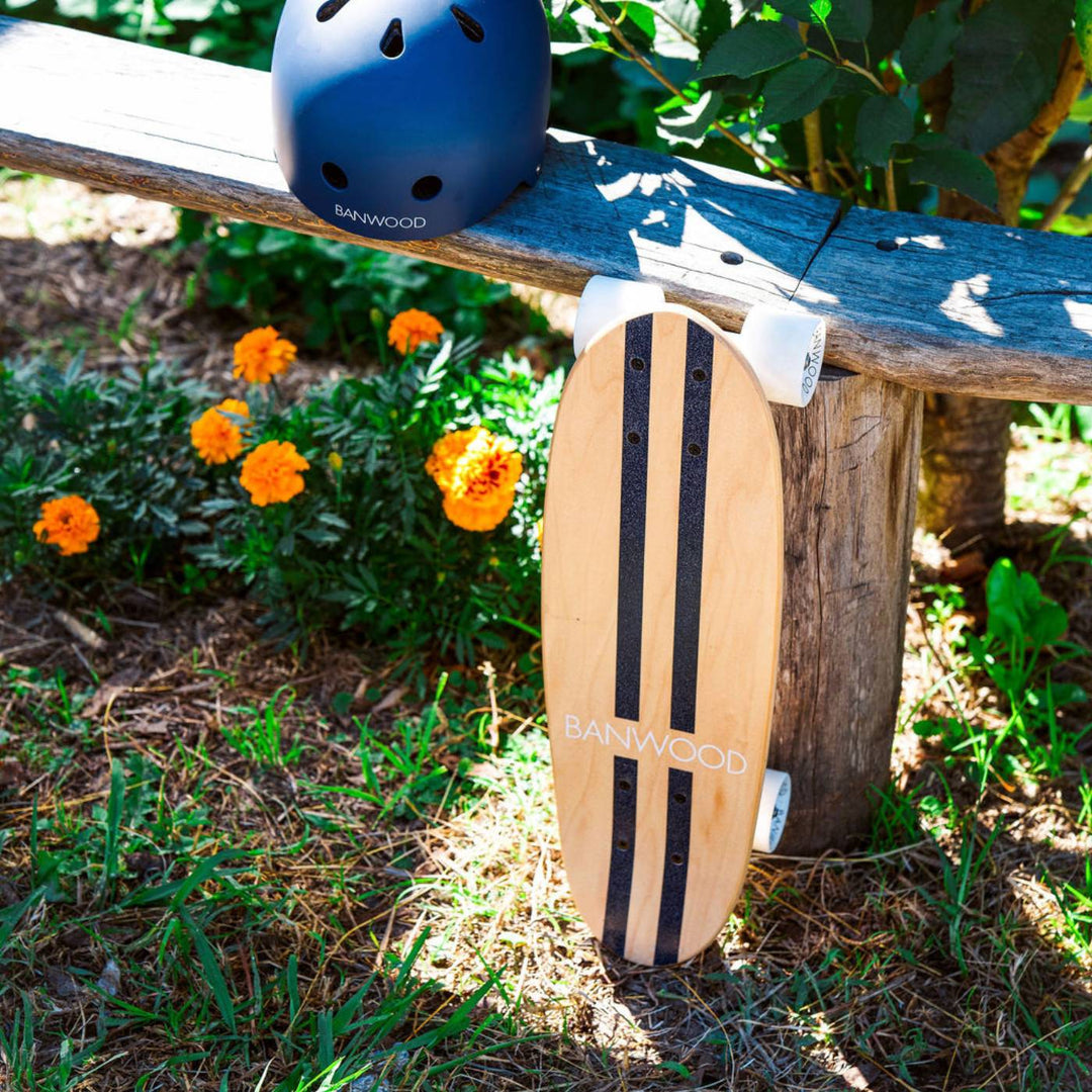 Banwood skateboard positioned on log with garden background and helmet