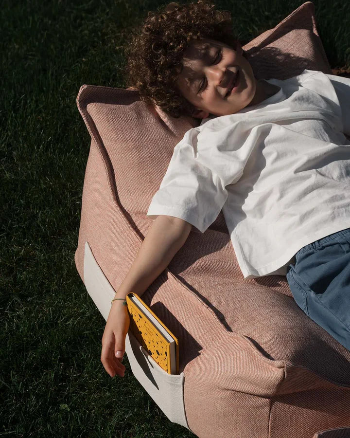 Pink bean bag chair with footrest section, child lounging on grass