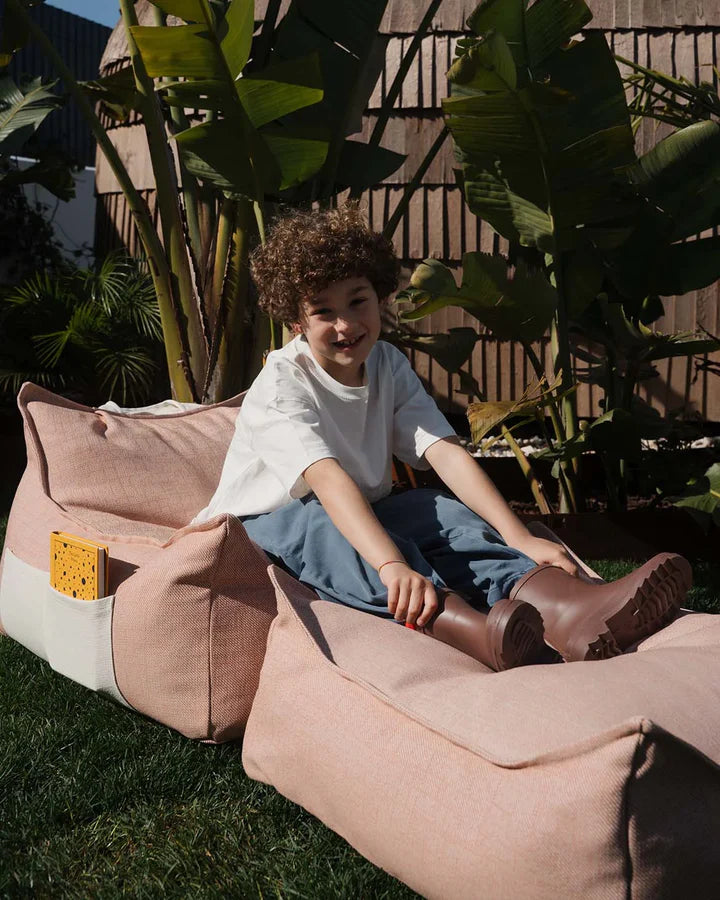 Child sitting in beige bean bag chair in sunny courtyard with palms