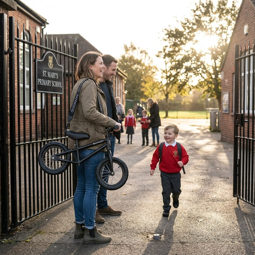 Parent at the school gate with a black Banwood balance bike carried on the shoulder strap