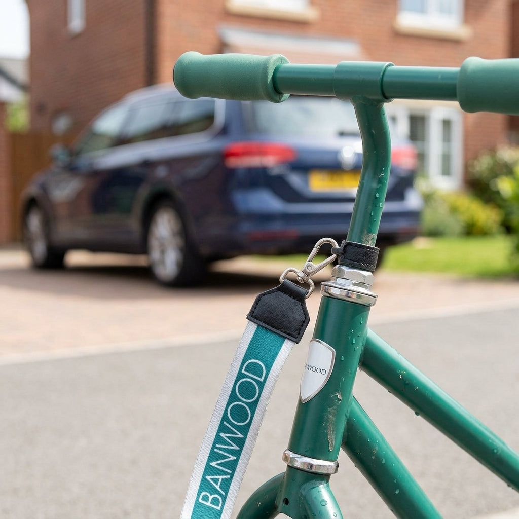 Close-up of the green Banwood carry strap clip fastened to a scooter frame on a driveway