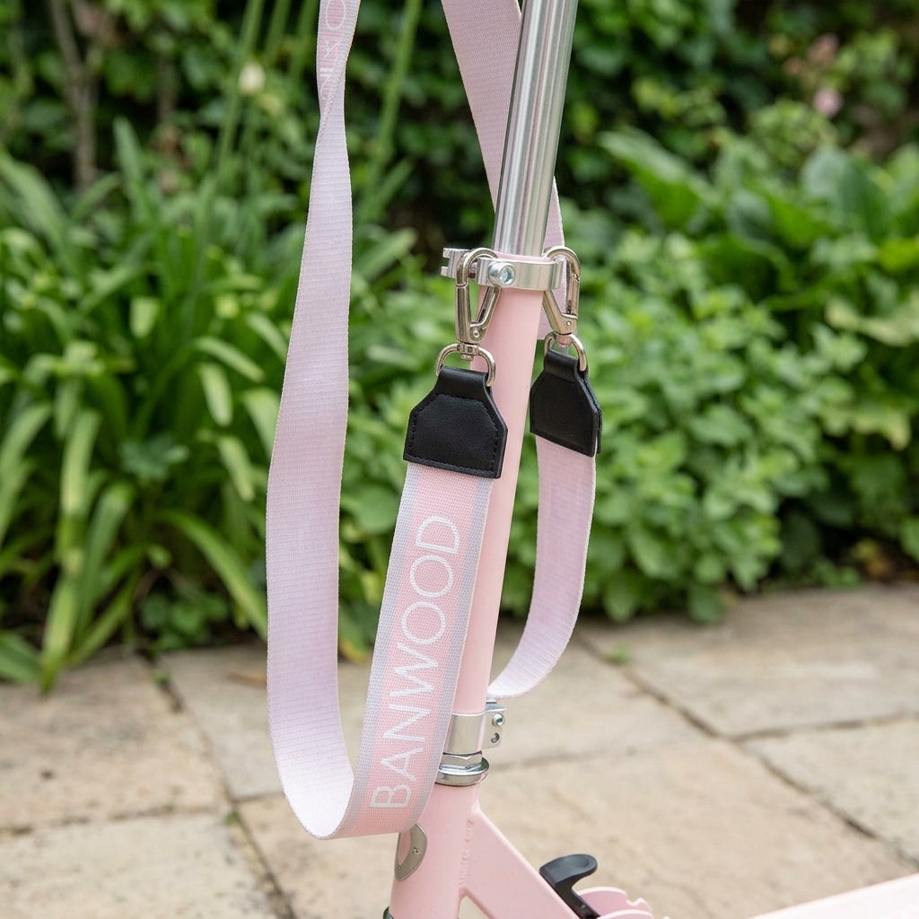 Close-up of the pink Banwood carry strap clip fastened to a scooter frame in a garden