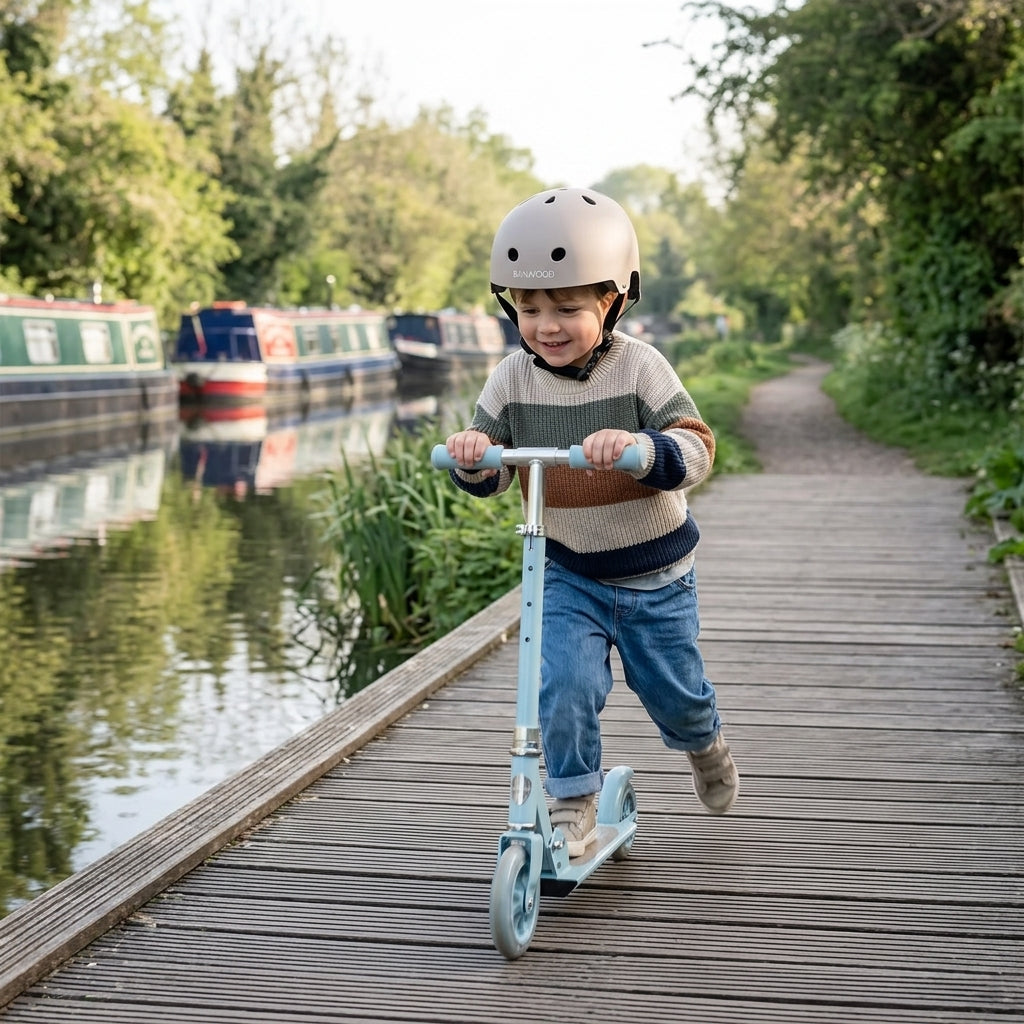 Child scootering along a canal towpath wearing the Banwood Classic Helmet in matte beige